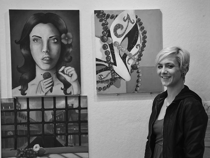Junior history major Jacquie DeLucca poses in front of her paintings on display in Bedford Hall.