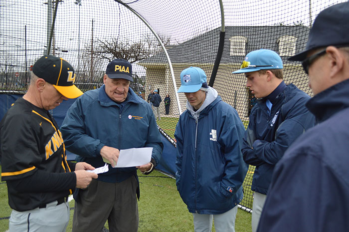 Home plate umpire Harry Kaskey, center-left, reviews line up cards at a plate conference with coaches.