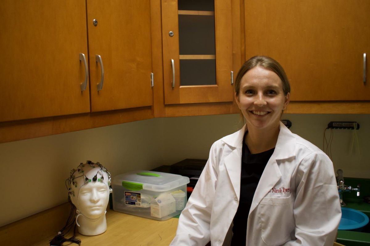 Dr.+Nicole+Ryerson+smiling+with+neuroscience+equipment+used+for+tracking+neurons+and+other+brain+data.