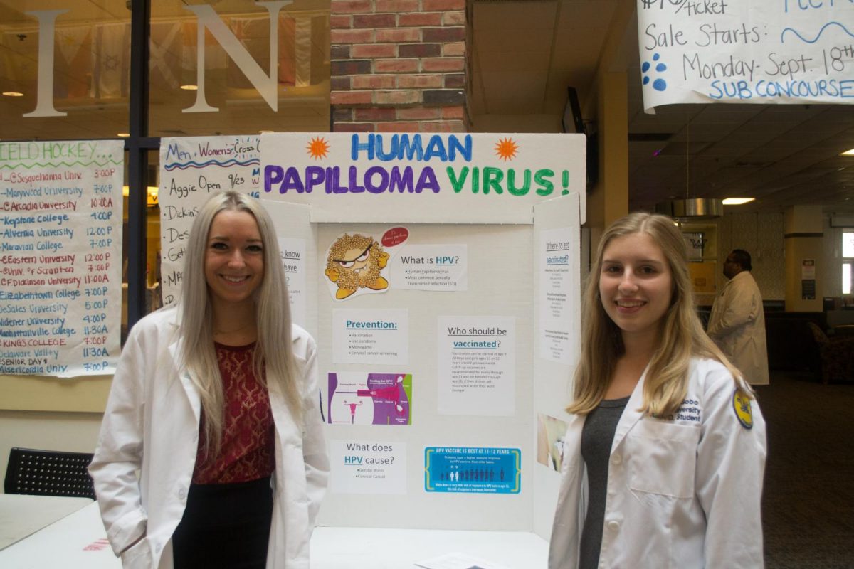 Pharmacy students Katie Miller, left, and Antonia Gobo, right, stand in front of their display on the human papilloma virus, a sexually transmitted disease. 