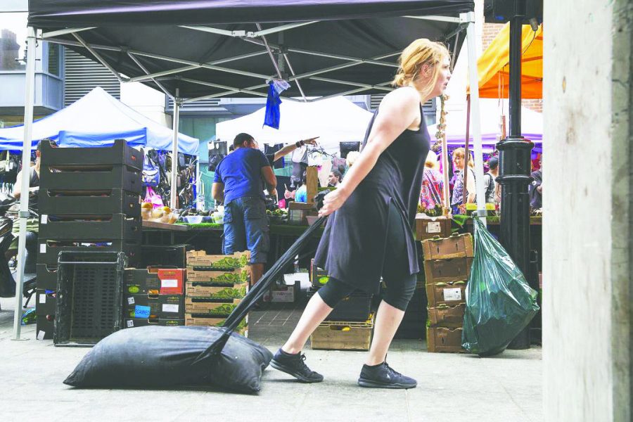 Heather Sincavage performing her performance piece, “The Burden of This.”  Sincavage carries her body weight in manure to signify the way living with trauma feels. 