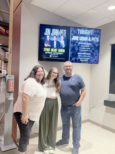 Sophomore Samara Carey stands beside her parents Shawn and Sue Carey as a “Jon, John and Pete” graphic is displayed on a television behind them.